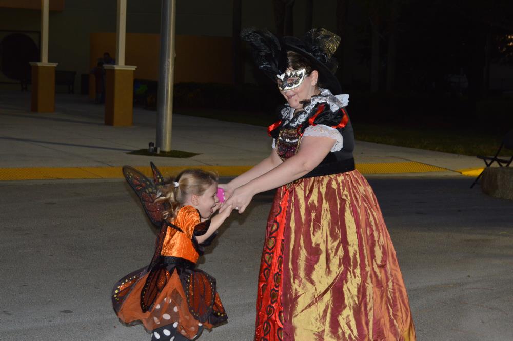 Woman in intricate dress and mask dances in street with girl in monarch butterfly dress